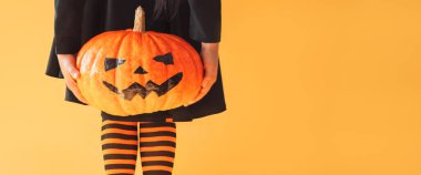 Siyah elbiseli çocuk ve çizgili diz boyu balkabağı tutan yüzü kesilmiş.