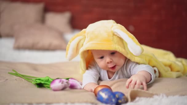 Baby lies in yellow bunny costume and plays with Easter eggs — Video