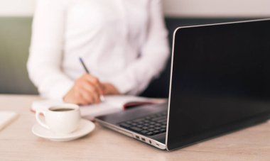 Kadın dizüstü bilgisayar ve kahve önünde kalemle yazıyor..