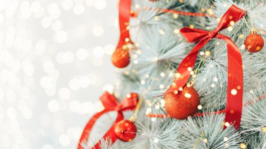 Kırmızı fiyonklarla süslenmiş Noel ağacı ve parlak arka planda takılar.