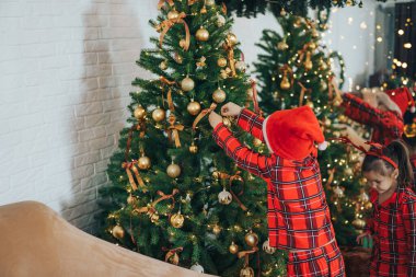 Aynı pijamaları giyen çocuklar Noel ağacını süslüyor..