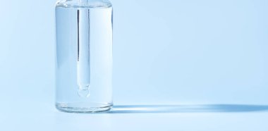 Mavi arka planda şeffaf sıvı pipetli cam kavanoz.