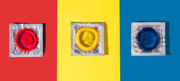 Three condoms of different colors on colorful background — Stok fotoğraf