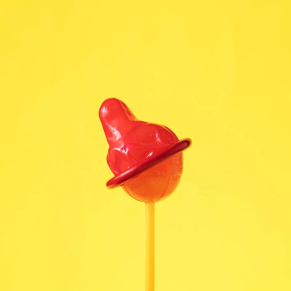 Lollipop with red condom against yellow background — Fotografia de Stock