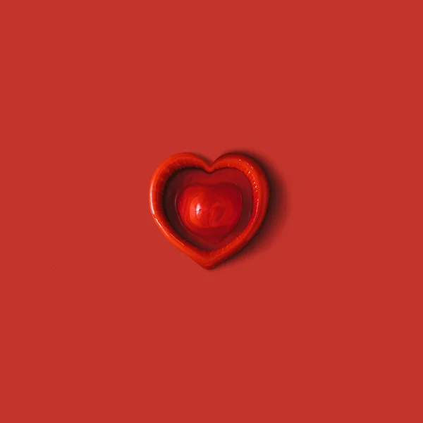 Розпакований червоний презерватив у формі серця на червоному тлі — стокове фото