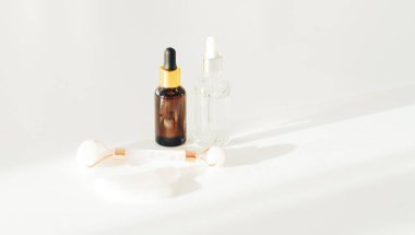 Beyaz arka planda pipetli cam şişeler ve masaj rulosu.