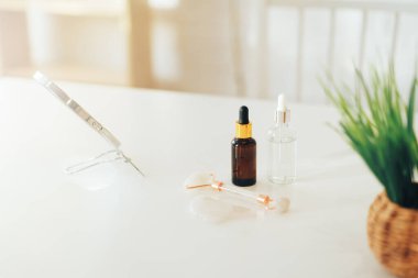 Aynanın yanında pipet ve masaj rulosu olan cam şişeler ve beyaz arka planda çimenler.