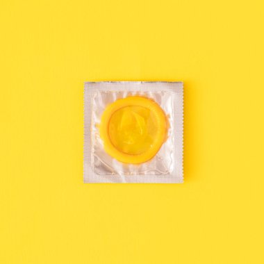 Sarı arka planda şeffaf pakette sarı prezervatif
