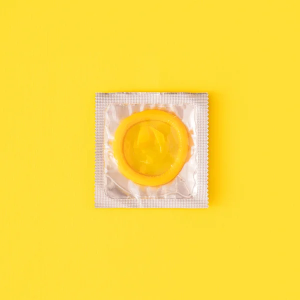 Żółta prezerwatywa w przezroczystym opakowaniu na żółtym tle — Zdjęcie stockowe