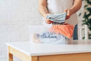 Kız kullanılmış giysileri yazıt bağışıyla birlikte plastik kutuya koyuyor.