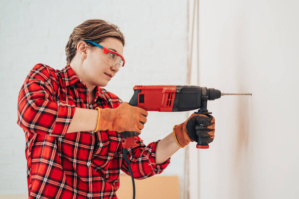 Laborer girl drilling concrete wall with drill