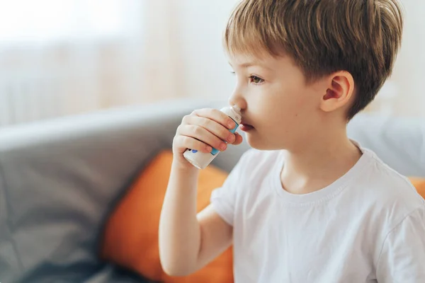 Menino usa spray nasal hormonal enquanto está sentado no sofá — Fotografia de Stock