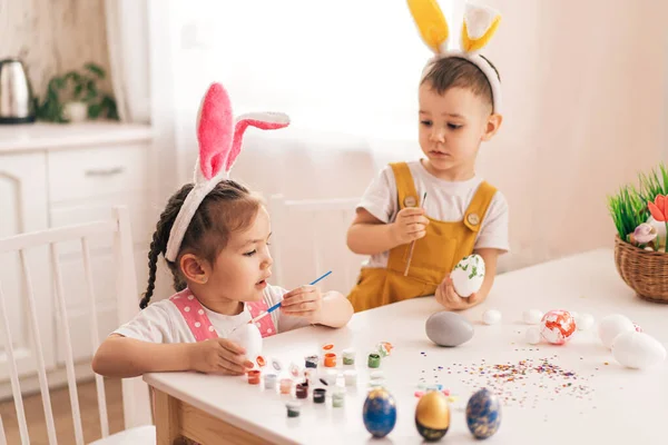 Смешные дети в кроличьих ушах красят яйца — стоковое фото