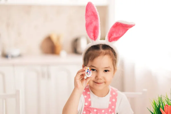 Ребенок в кроличьих ушах держит украшенное яйцо в руках — стоковое фото