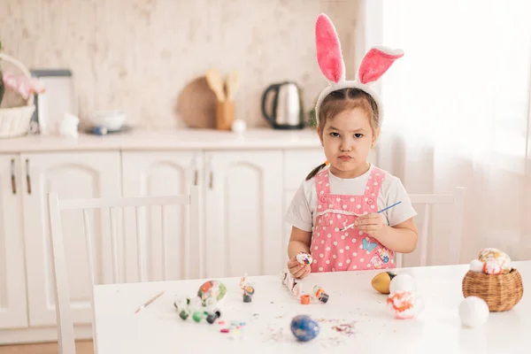 Девушка в кроличьих ушах готовится к Пасхе, украшая яйца — стоковое фото