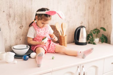 Küçük çocuk yumurtaları farklı renklerde boyar.