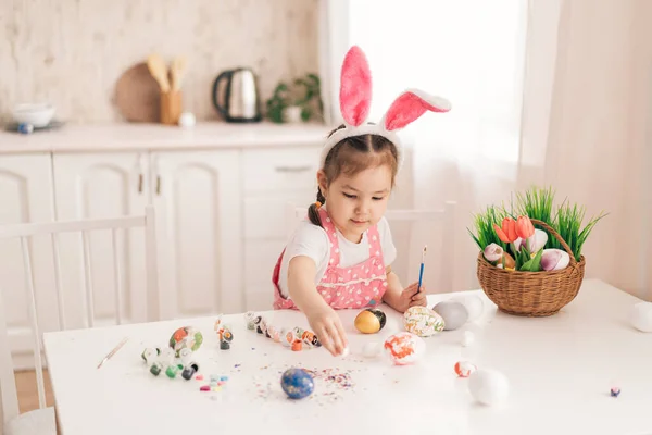 Ребенок в кроличьих ушах рисует яйца за столом — стоковое фото