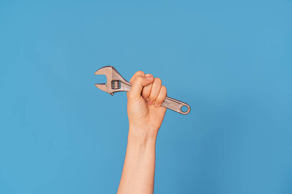 Womans hand with an adjustable wrench against blue background