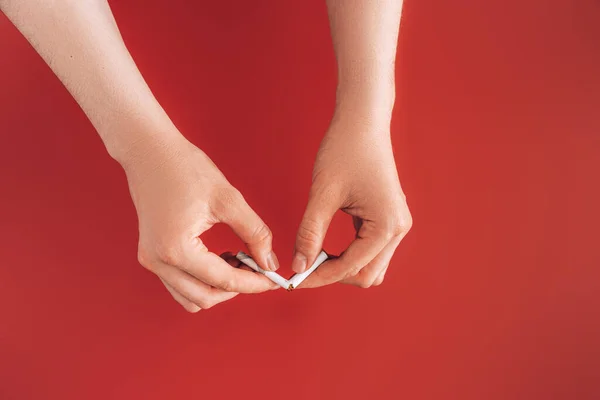 Manos rompiendo el cigarrillo por la mitad contra fondo rojo — Foto de Stock