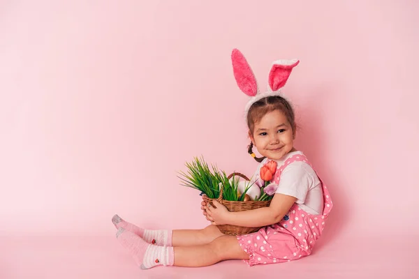 Ребенок с корзиной в руках сидит на розовом фоне — стоковое фото