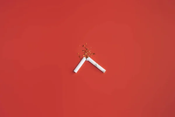Kırmızı arka planda kırık sigaradan tütün yarıya dökülüyor. — Stok fotoğraf
