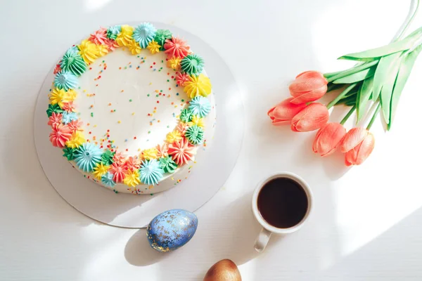 Пасхальний торт, прикрашений різнокольоровими вершками поруч з тюльпанами та яйцями — стокове фото