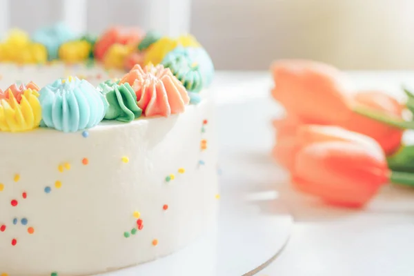 Lalelerin yanında çok renkli kremayla süslenmiş beyaz pasta. — Stok fotoğraf