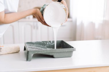 Girl pours white paint from can into ditch