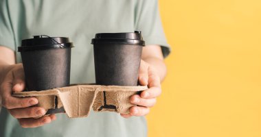 Yeşil tişörtlü kız sarı arka planda sıcak çay bardakları tutuyor