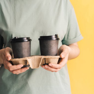 Yeşil tişörtlü kız elinde fincanlarla sarı arka planda.