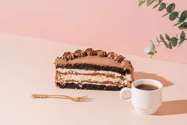 Half of sliced cake next to fork and cup of coffee on pink background — стоковое фото
