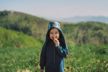 Pilot kostümlü kız yeşil dağların ve açık gökyüzünün önünde duruyor.