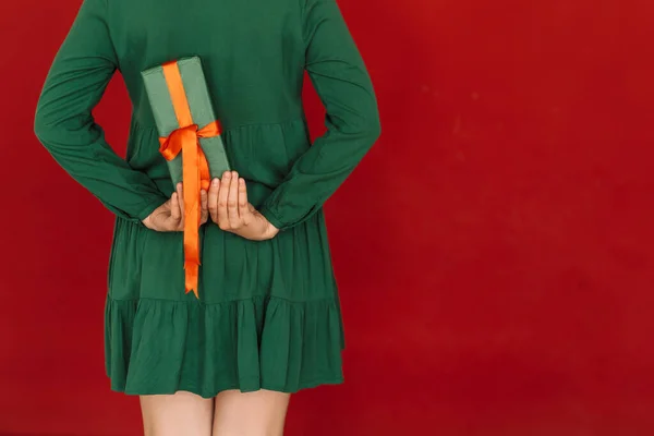 Girl in green dress holds gift behind her against red background — Fotografia de Stock