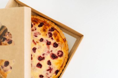 Üzerinde çilekli turta olan açık bir kutu beyaz masada duruyor..