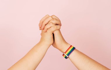 İki kadın eli pembe bir arka planda birbirini tutuyor..