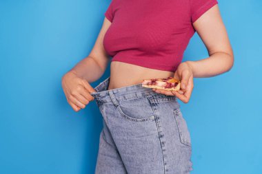 Kız elini mavi arka plana uzatarak kot pantolon giyiyor..