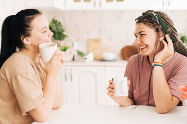 Mutfakta masada oturmuş içki içerken iki kız konuşuyor..