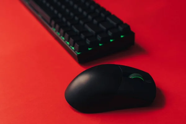 Computer wireless gaming mouse and keyboard with green backlight against red background.