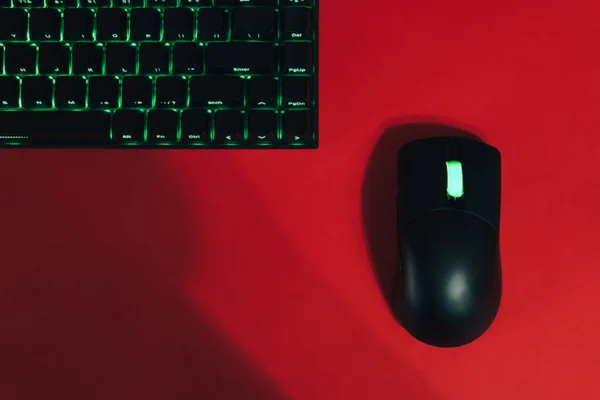 Computer wireless gaming mouse and keyboard with green backlight against red background.