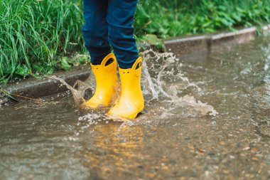 Boy in yellow rubber boots jumping in puddles.