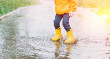 Child in yellow rubber boots jumping through puddles.