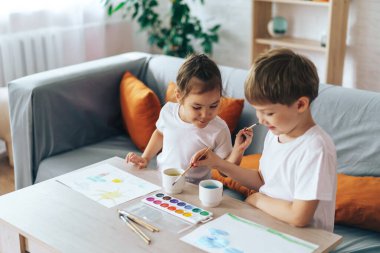 Children paint nature on sheets while sitting at the table.