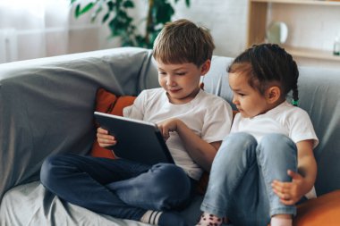 Boy and girl sitting on the couch watching video on the tablet.