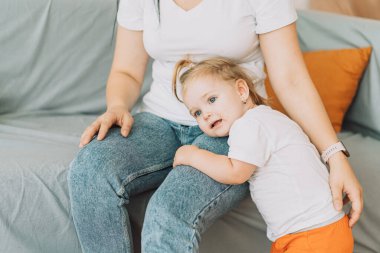 Little girl put her head on her mothers leg.