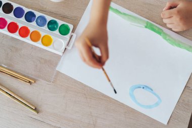 Child paints green grass and blue sky.