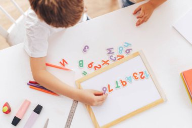 Schoolchildren study letters and lay them out hardly sitting at the table.