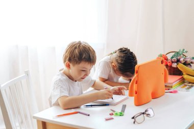 Children draw in a notebook and watch a lesson on a tablet.
