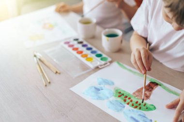 Children paint green grass with a tree and blue clouds.