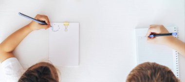 A boy and a girl draw with a blue pen in notebooks.