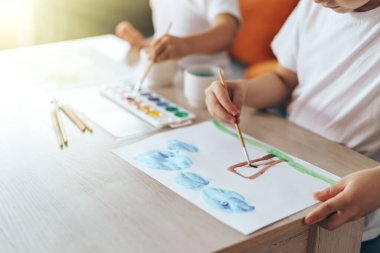 Children paint green grass with a tree and blue clouds.